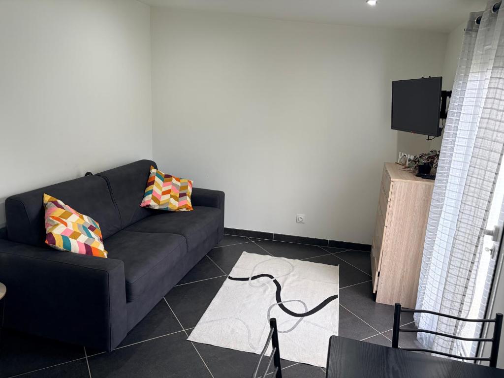 a living room with a black couch and a tv at Studio 2 - Loc Conciergerie in Trappes