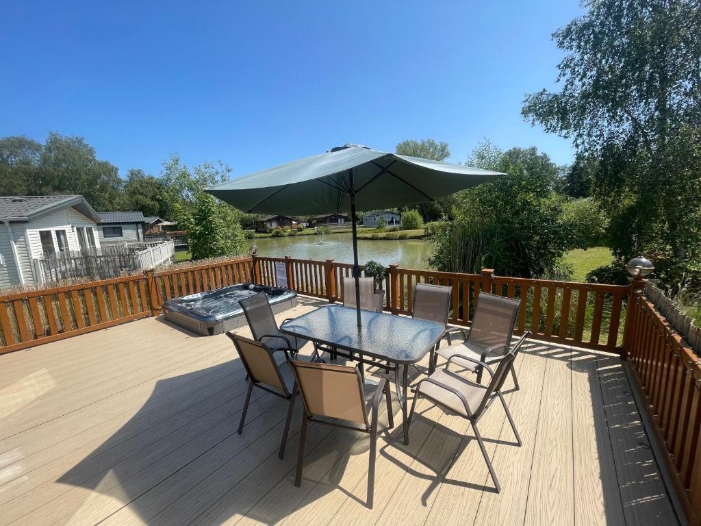 a table and chairs with an umbrella on a deck at Luxury Lakeside Lodge L1 with hot tub situated at Tattershall Lakes Country Park in Tattershall