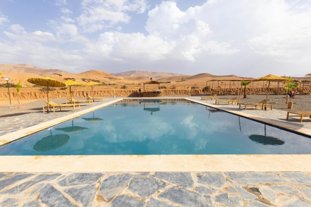 a large pool with chairs and mountains in the background at Be Nomad Agafay Camp in El Karia