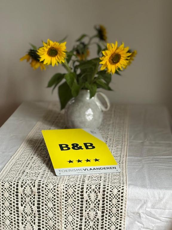 a yellow sign on a table with a vase of flowers at Snow&Rose in Damme