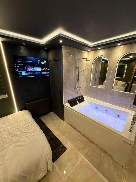 a bedroom with a tub and a bed and a television at Onyx Suite Jacuzzi Privatif in Villejust