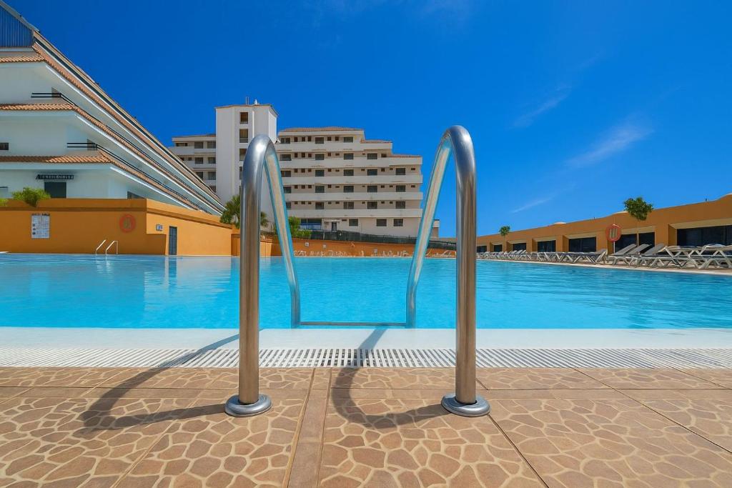 a swimming pool with two metal handles in front of a building at Apto Jardin del Sol Beach-Pool in Puerto de Santiago