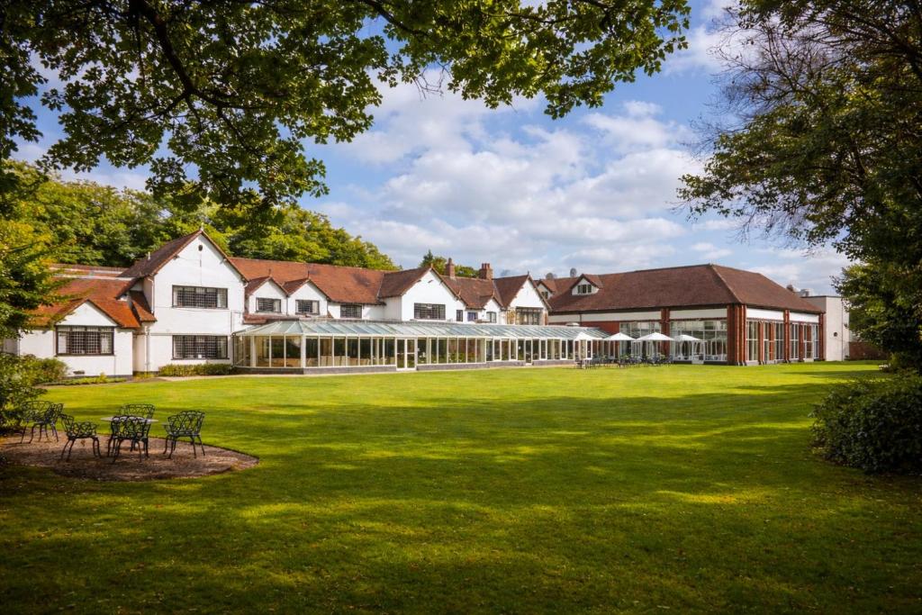 a large building on a green lawn with chairs at Macdonald Craxton Wood Hotel & Spa, Chester in Ledsham