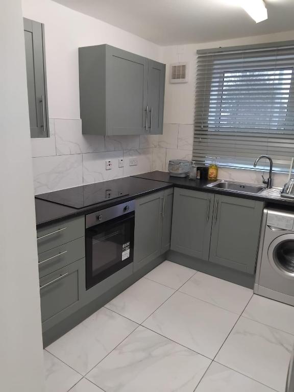a kitchen with gray cabinets and a sink and a dishwasher at Robin's Accommodation in Wythenshawe