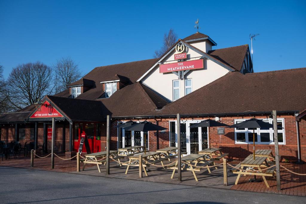 a restaurant with chairs and umbrellas in front of a building at Weathervane Hotel by Greene King Inns in Stoke on Trent
