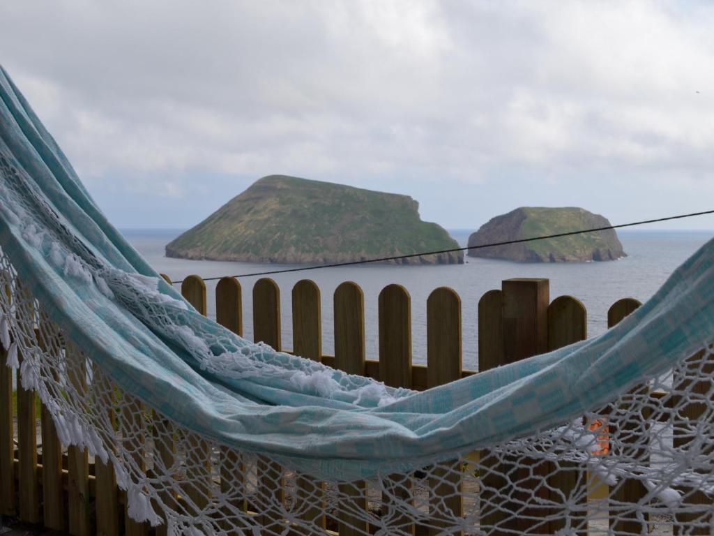 a hammock on the beach with two islands in the water at Casinha de Muda da Feteira in Angra do Heroísmo