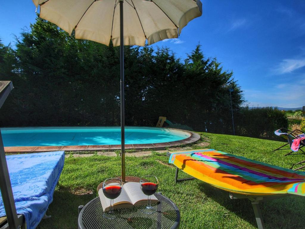 a table with a glass of wine and an umbrella next to a pool at Belvilla by OYO Camillo Tosco in Valiano