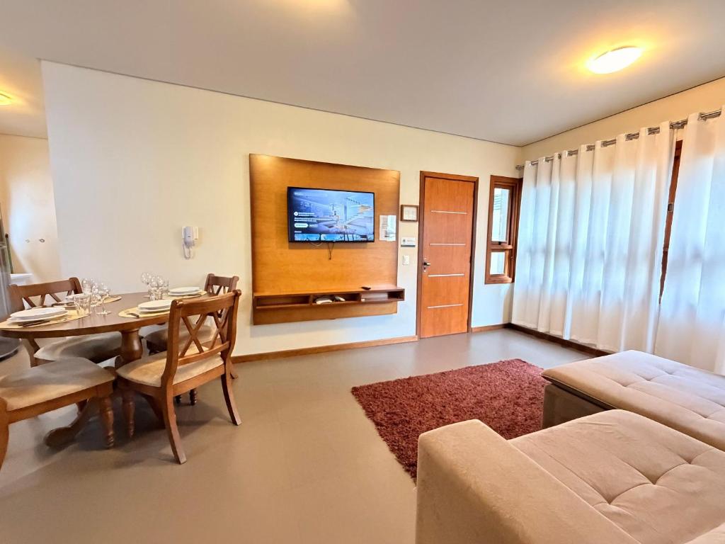 a living room with a table and a tv on the wall at Apto Rua Coberta Gramado in Gramado