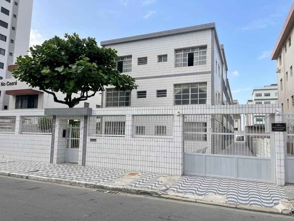 a white building with a tree in front of it at Apto no Canto do Forte com garagem in Praia Grande