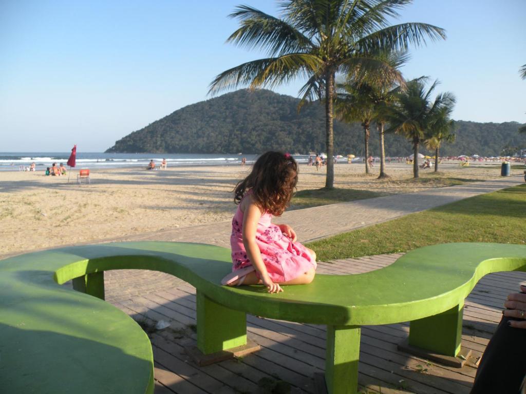 a little girl sitting on a green bench at the beach at Casa Villaggio Beira-mar in Bertioga