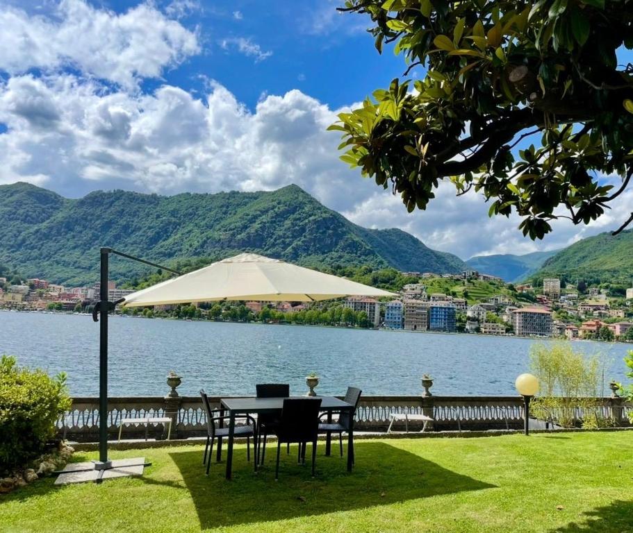 a table with chairs and an umbrella next to a lake at Exclusive-LakeView Bella Vista Orta G&G in Omegna