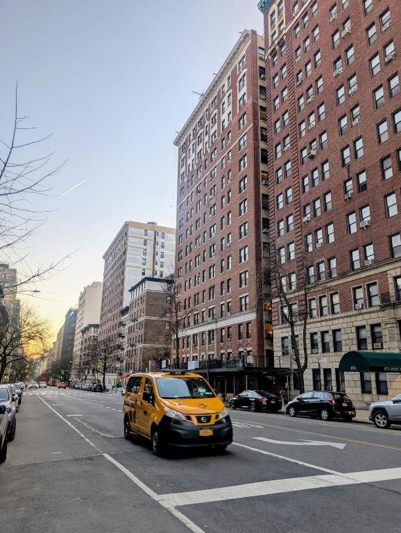 a yellow van driving down a city street with buildings at MANHATTAN ROSE Homestay in New York