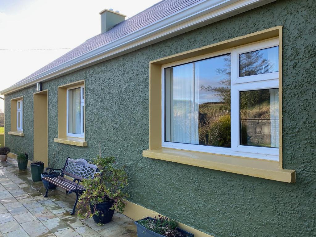 a green house with a window and a bench at Sea View Hideaway in Milltown Malbay