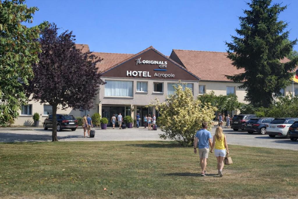 two people walking in front of a hotel at Hotel The Originals Bernay Acropole in Bernay