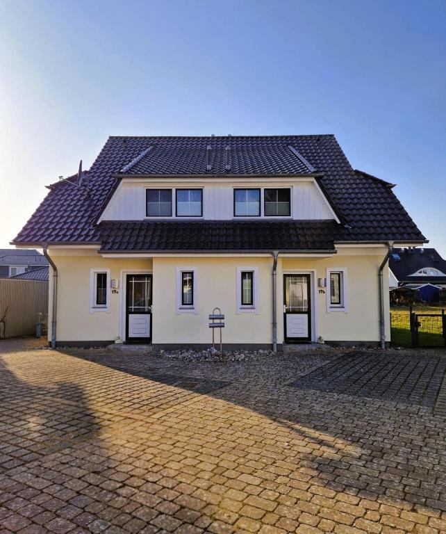 a white house with a black roof on a brick driveway at Strandstr_ in Zingst