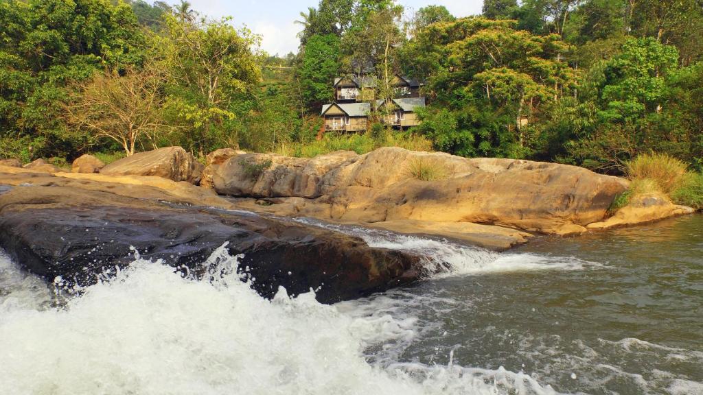 une rivière avec de l'eau se précipitant au-dessus d'une formation rocheuse dans l'établissement Moselberg Riverside Cottages, à Munnar