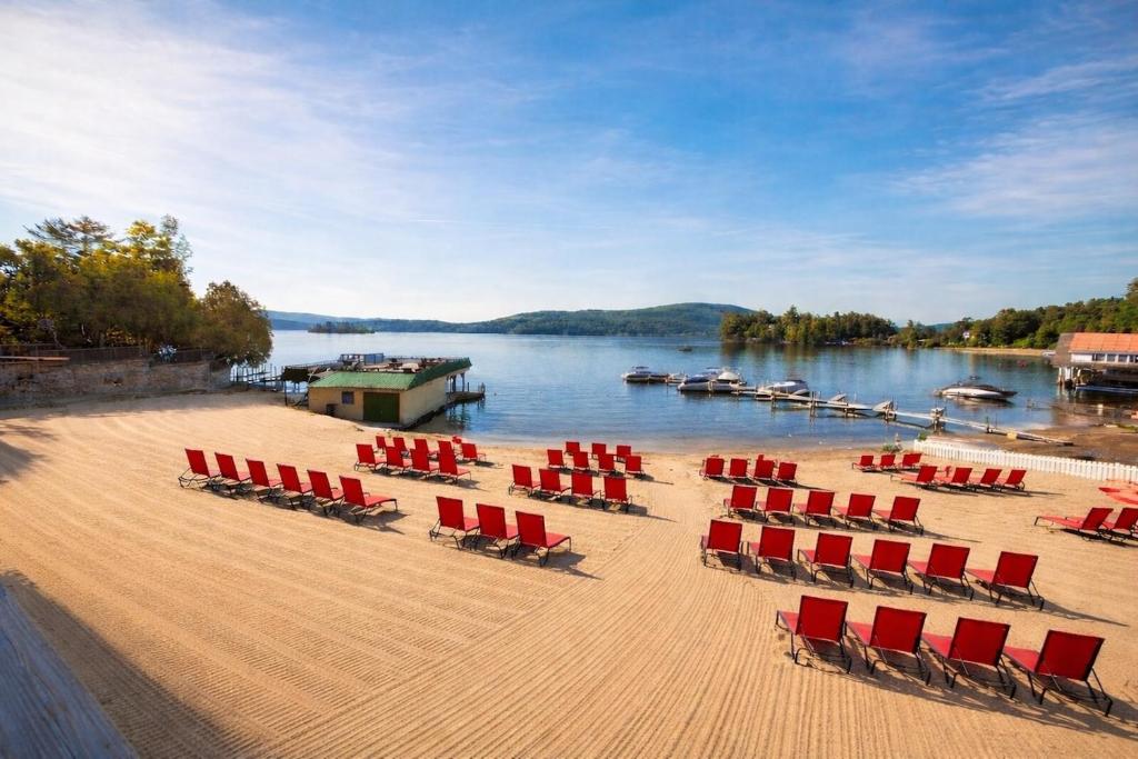 a beach with chairs and boats on the water at Depe Dene Lakeside Resort in Lake George