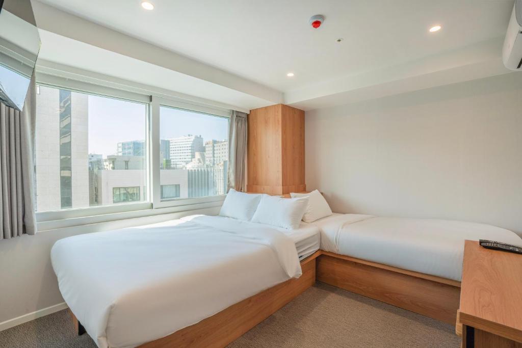 two beds in a room with a large window at KIMSTEL Jongno in Seoul