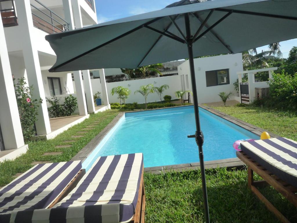 an umbrella and two lounge chairs next to a swimming pool at Hôtel Fitiavana in Nosy Be