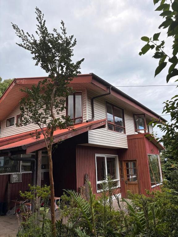 a red house with a tree in front of it at Refugio Urbano Melipulli in Puerto Montt