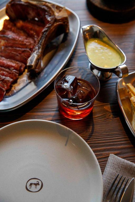 A close-up table setting presents plated meat, sauce and a drink.