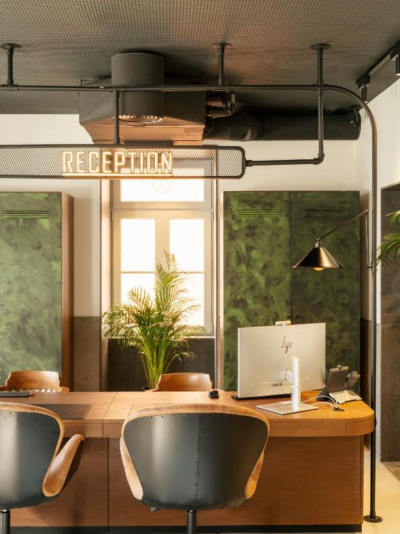 A reception and work counter with a desktop computer, chairs, and indoor plants.