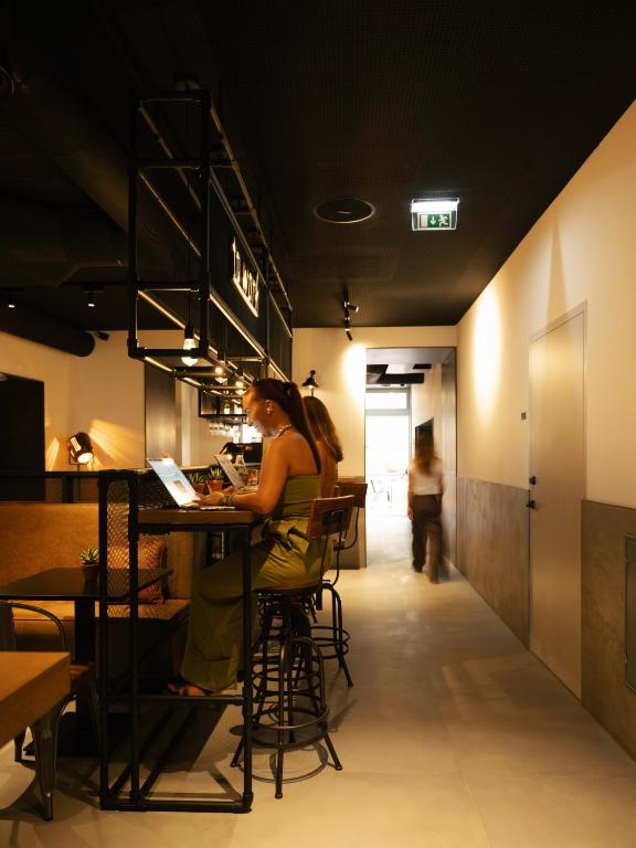 A high communal work counter runs along a hotel corridor beside the bar area.
