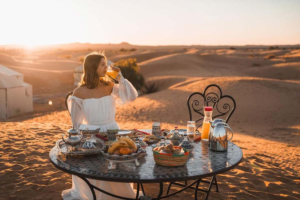 a woman sitting at a table in the desert at Elite Sahara Desert Camp in Merzouga