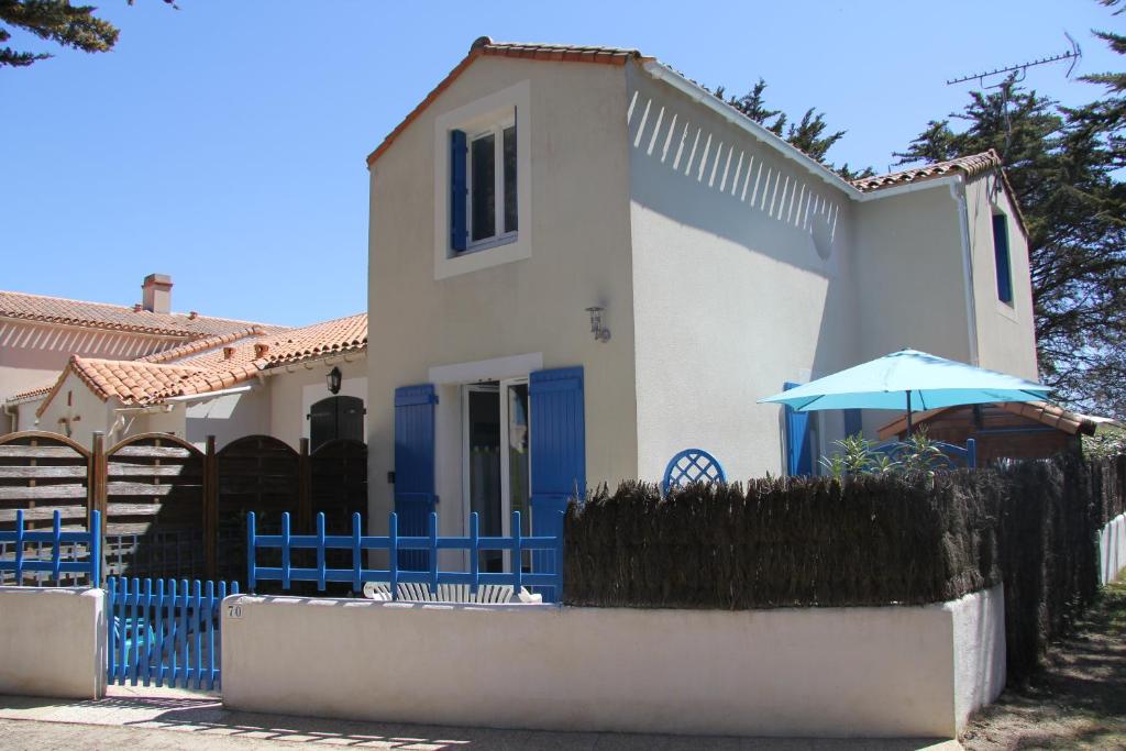 a white house with a blue fence and an umbrella at Un petit coin de paradis in Barbâtre