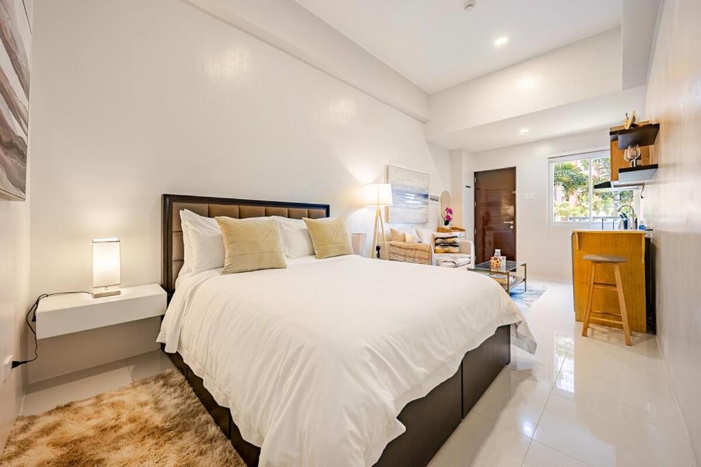 a white bedroom with a large bed and a window at Cara Studio Mactan Cebu Cozy with Garden View at Primeworld District Tower H 103 in Lapu Lapu City