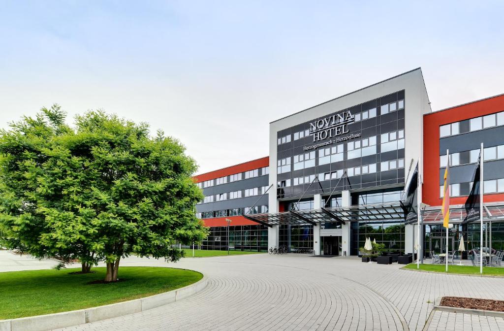 a large building with a tree in front of it at Novina Hotel Herzogenaurach Herzo-Base in Herzogenaurach