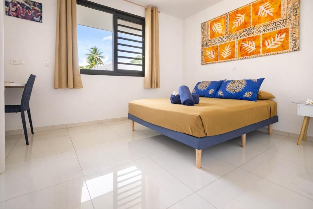 a bedroom with a bed with blue pillows and a table at Fare Re'are'a - Charmant bungalow côté mer proche de la plage de Temae in Moorea
