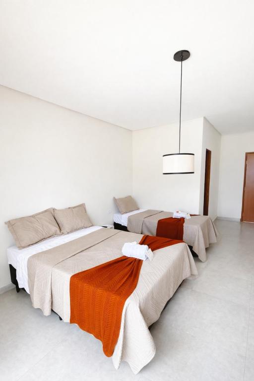 a white room with three beds with orange blankets at Pousada Iraquara in João Pessoa