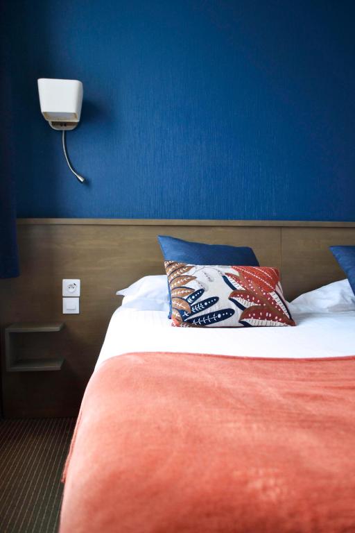 a bed with two pillows and a blue wall at Brit Hotel Le Surcouf in Saint Malo