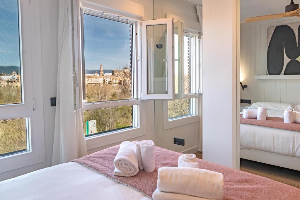 a bedroom with a bed and windows with towels at Geysotur Ribera Luxury Suites in Córdoba