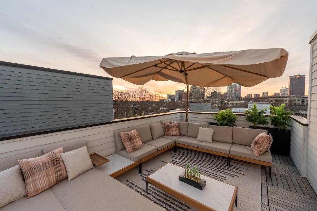 a patio with a couch and an umbrella on a balcony at Sleeps 8 - Rooftop Deck - Prime Location in Raleigh