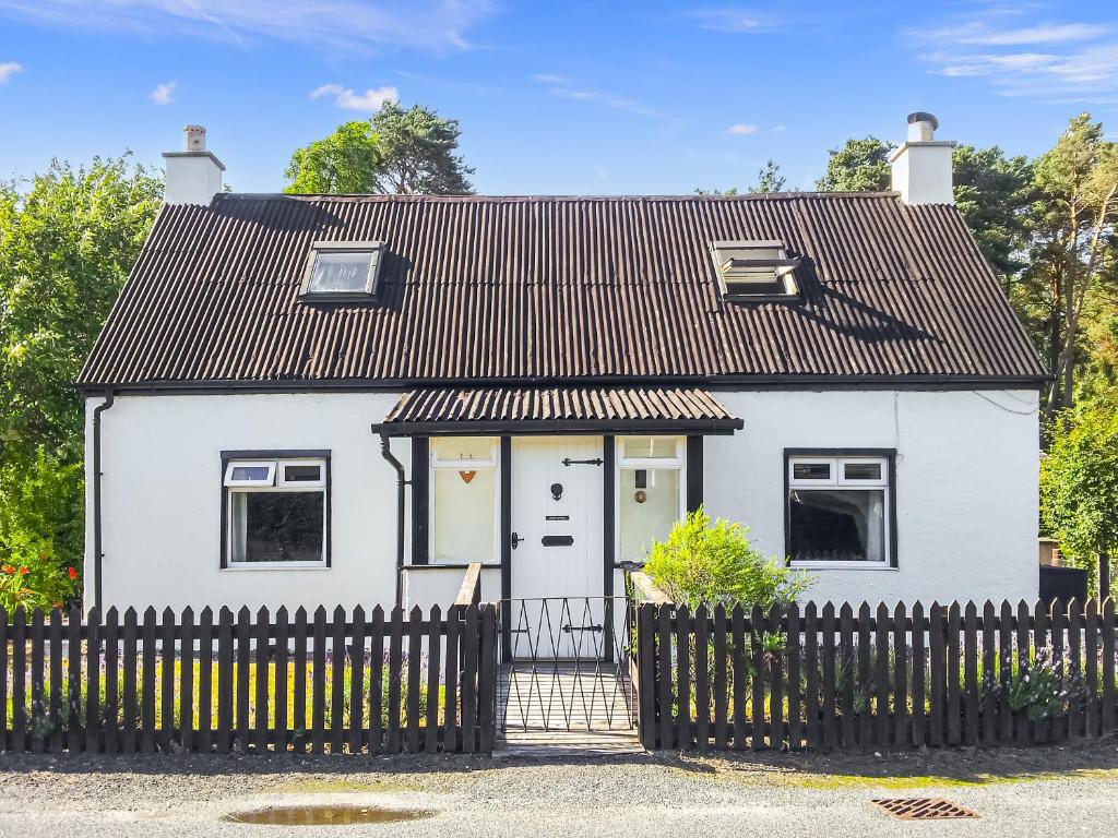 a white house with a black roof and a fence at Broom Cottage in Newtonmore