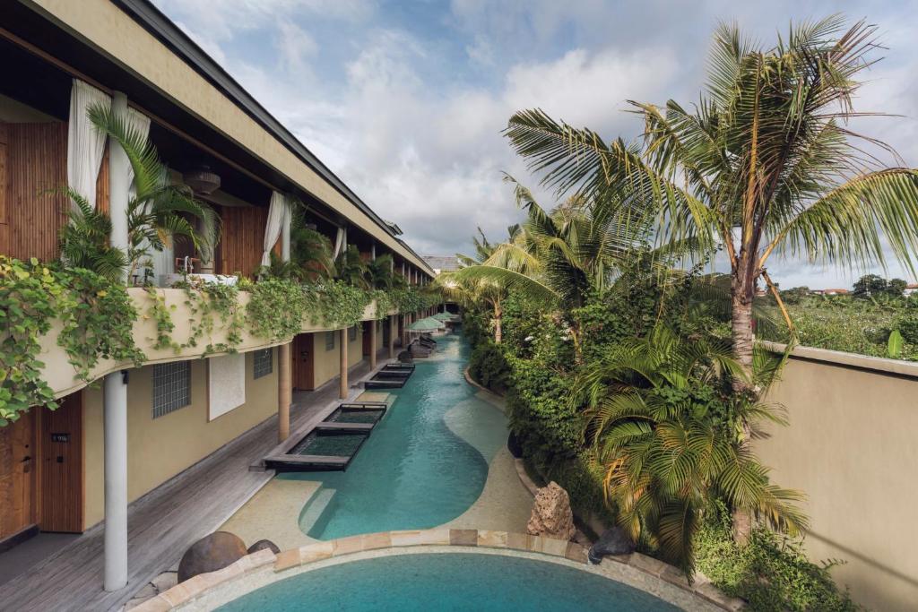a hotel corridor with a swimming pool and palm trees at Sini Vie Resort & Spa Seminyak by Ini Vie Hospitality in Seminyak