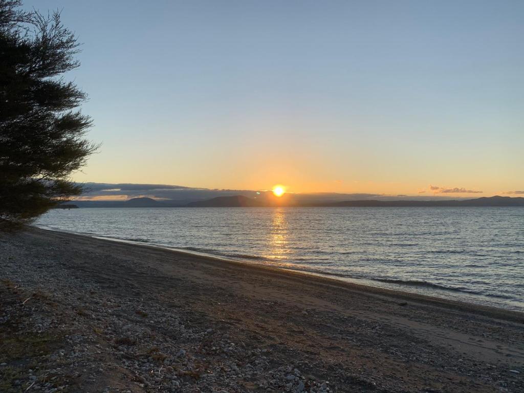 a sunset on a beach with the sun in the distance at Lake Views, Ani Miria Place, Te Rangiita, Turangi in Turangi
