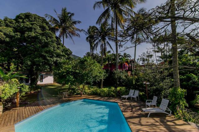 una piscina con 2 sillas blancas y árboles en Ilhabela Homestay, en Ilhabela