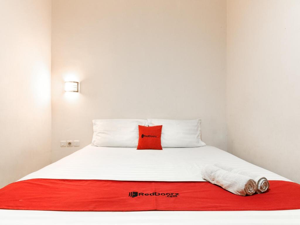 a white bed with a red pillow and a red blanket at RedDoorz @ Pandu Raya Bogor in Bogor