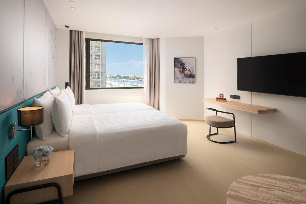 A bright bedroom with a window view, wall-mounted television and a narrow writing desk.