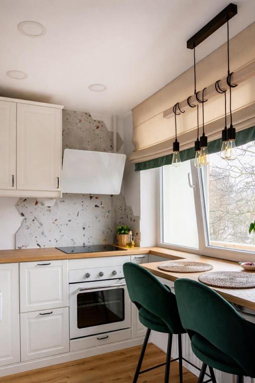 a kitchen with white cabinets and a table with green chairs at Cozy Apartment Mazeikiai in Mažeikiai
