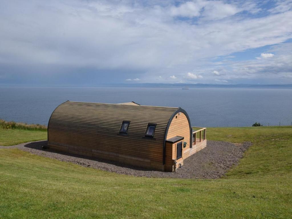a large wooden building in a field next to the water at 2 Bed in Tain oc-81339 in Nigg
