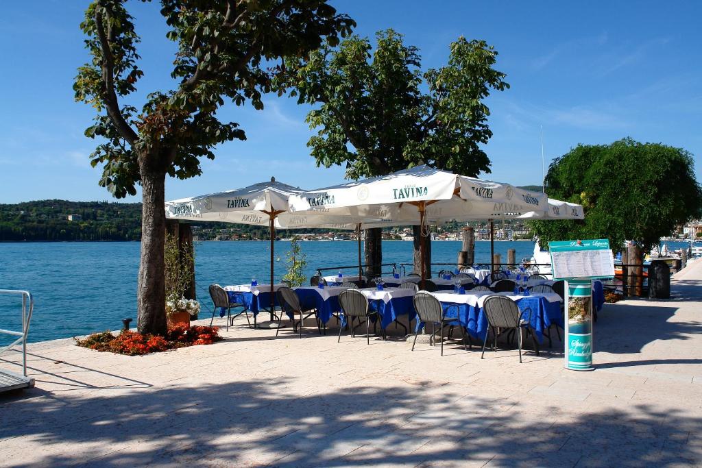 un groupe de tables avec chaises et parasols à côté de l'eau dans l'établissement Hotel Ristorante Lepanto, à Salò