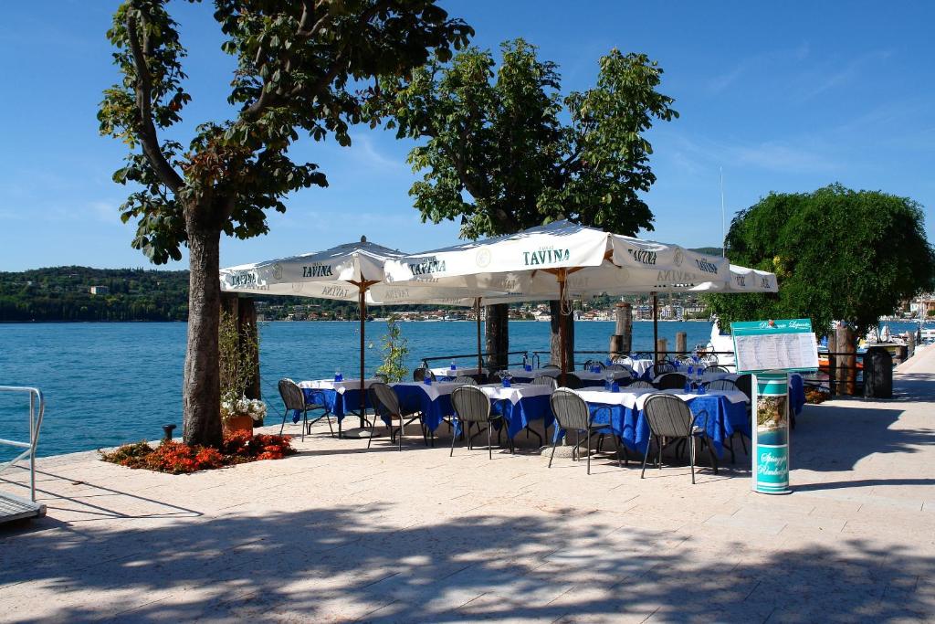 a group of tables with chairs and umbrellas next to the water at Hotel Ristorante Lepanto in Salò