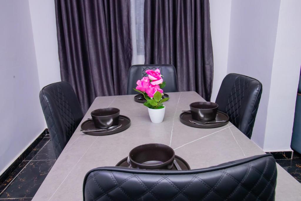 a table with black chairs and a pink flower on it at Living Space Service Apartment in Mama