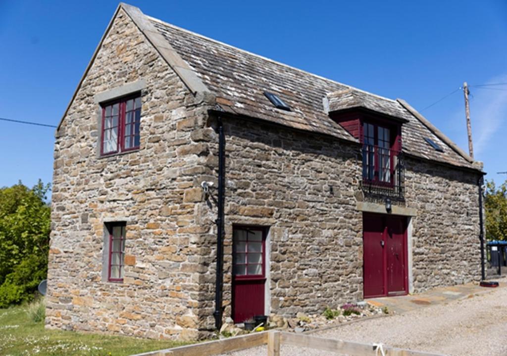 an old stone building with red doors and windows at Craiglea Barn in Latheron
