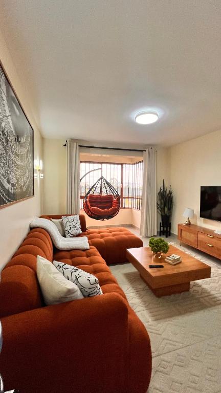 a large living room with orange couches and a table at Midtown LakeView 2BR House with Heated pool, Netflix, 24Hr security & reception -Shawmut Nakuru in Nakuru