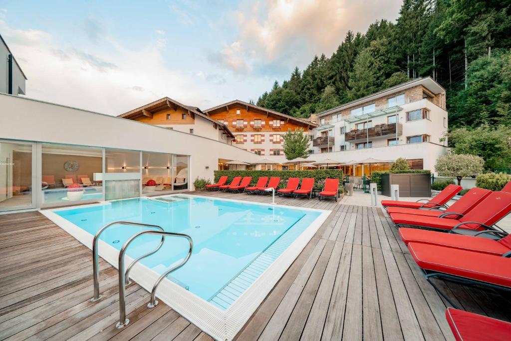 ein Schwimmbad mit roten Stühlen und ein Gebäude in der Unterkunft Familotel Amiamo in Zell am See